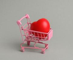 red heart in a miniature metal trolley from the store on a gray background photo