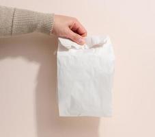 female hand holds a full paper bag on a beige background. Refusal from plastic packaging, food delivery photo