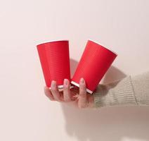 hand holds paper cardboard red cups for coffee, beige background. Eco-friendly tableware, zero waste photo