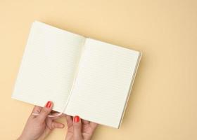 dos manos femeninas sostienen un cuaderno abierto con hojas blancas en blanco sobre un fondo beige foto