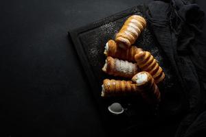 baked tubules filled with whipped egg white cream on a black wooden kitchen board, top view photo