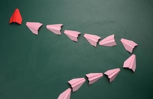 Group of pink paper airplanes following the first red on a green background photo