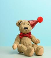 brown teddy bear in a red cap sits on a blue background, photo