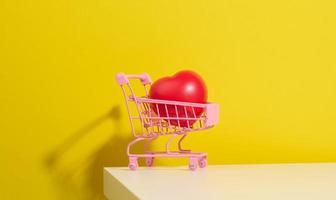 red heart in a miniature metal trolley from the store on a yellow background. Organ donation, transplant concept photo