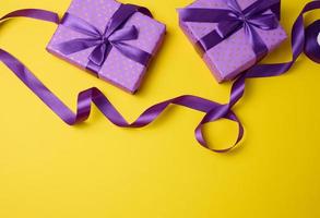 wrapped boxes in gift purple paper and silk ribbon on a yellow background, top view. Congratulations and surprise photo