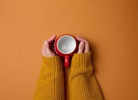 empty red ceramic cup in a female hand on orange background, drink and hand are raised up, coffee break photo
