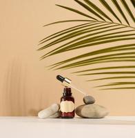 a brown glass bottle with a pipette and a brown label stands on a stone. Container for cosmetics, serum and oil. Palm leaf shadow photo