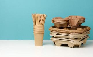 a stack of brown disposable paper cups and a stand on a white table, blue background photo