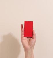 Female hand holding empty red paper on a beige background. Copy paste image or text, close up photo