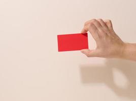 Female hand holding empty red paper on a beige background. Copy paste image or text, close up photo