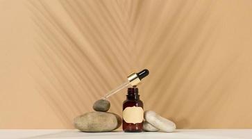 a brown glass bottle with a pipette and a brown label stands on a stone. Container for cosmetics, serum and oil. Palm leaf shadow photo