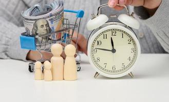 wooden figurines of a family, a female hand holds an alarm clock on a white table. Concept time is money, budget planning. Time to pay debts photo