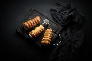 baked tubules filled with whipped egg white cream on a black wooden kitchen board, top view photo