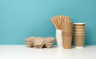 a stack of brown disposable paper cups and a stand on a white table, blue background photo