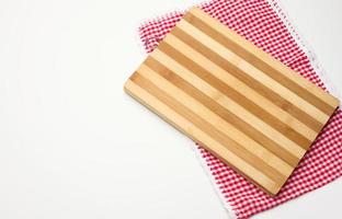 tabla de cortar de cocina de madera rectangular vacía y toalla roja en una jaula blanca sobre una mesa blanca, vista superior foto