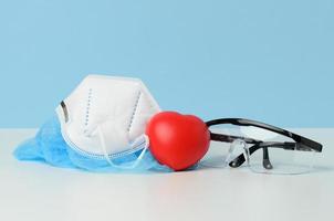 gafas médicas protectoras de plástico transparente y máscara desechable blanca sobre fondo azul foto