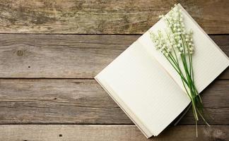 open notebook with blank white sheets and a bouquet of blooming lilies of the valley on a wooden table from gray boards, top view photo