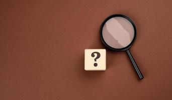 black magnifier on a brown background and question marks. The concept of uncertainty and the search for solutions photo