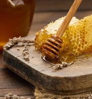 panal de cera con miel sobre una tabla de madera, detrás de un tarro de miel foto