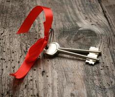 dos llaves de la puerta de la casa de metal con cinta roja sobre un fondo de madera