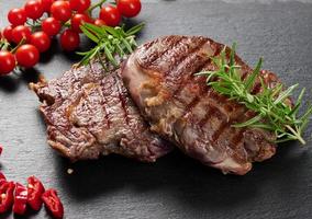 two fried ribeye beef pieces on a black slate board, rare degree of doneness. Appetizing steak