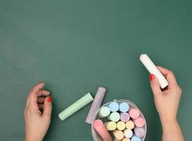 hand holds a piece of white chalk on the background of an empty green chalk board photo