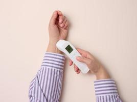 process of measuring body temperature on the wrist with a non-contact thermometer, beige background photo