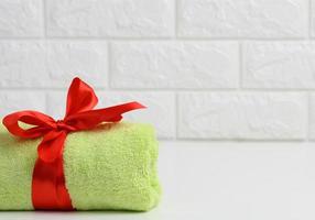 rolled up terry green towel tied with red silk ribbon on white shelf in bathroom, copy space photo