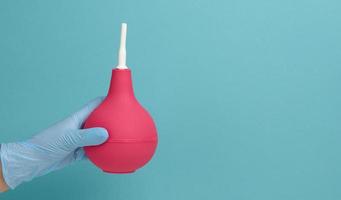 a hand in a blue medical glove holds a pink rubber enema on a blue background photo