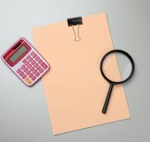 pink calculator, folder with blank  sheets and black magnifier on a gray background photo