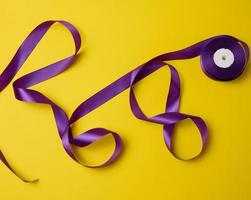twisted purple textile ribbon for decoration on a yellow background, flat lay photo