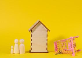 wooden house and metal miniature cart on a yellow background. Real estate purchase concept photo