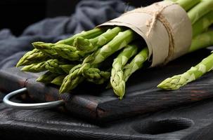 manojo de espárragos crudos frescos en una tabla de cocina negra de madera foto