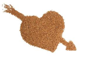 heap of uncooked buckwheat grains, top view. Groats laid out in the shape of a heart and isolated against white background photo