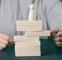 woman's hand pulls out a wooden block from the tower on which the figurine stands. The concept of reputational risks photo