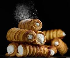 Baked tubules filled with whipped egg whites cream on a black wooden kitchen board photo