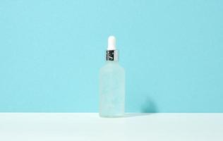 white glass bottle with pipette stands on a blue background. Cosmetics SPA branding. Packaging for gel, serum, advertising and product promotion, mock up photo