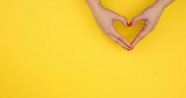 two female hands folded in the shape of a heart on a yellow background. Gratitude and kindness concept, banner photo