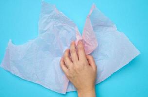 female hand hold pink folded wrapping crumpled paper on a blue background photo