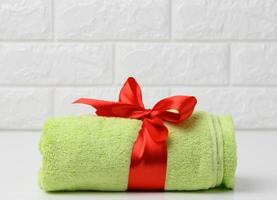 toalla verde terry enrollada atada con cinta de seda roja en un estante blanco en el baño foto