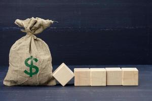 full brown canvas bag with US dollar icon and five wooden blank cubes on blue background. Wealth photo