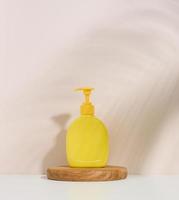 Yellow plastic container with a dispenser on a beige background. Yellow container for liquid soap, shampoo photo