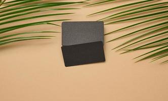 a stack of rectangular black paper business cards and a leaf of a palm tree on a brown background. View from above photo