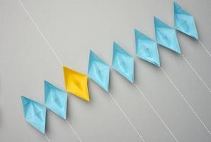 A row of paper boats on a gray background, yellow is moving in the opposite direction photo