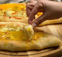 baked Adjarian khachapuri with whole egg yolk on a wooden board, hand beats a piece of bread into a spilled yolk photo