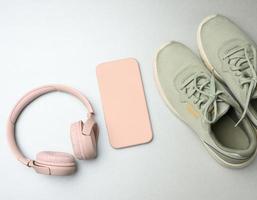 pair of pink sneakers, wireless headphones, a smartphone on a gray background. photo