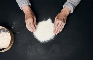 White wheat flour on a black table and two female hands, top view photo