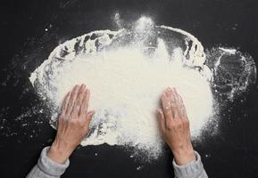 Sifted white wheat flour on a black table and two female hands, top view. cooking at home photo