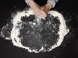 Sifted white wheat flour on a black table and two female hands, top view. cooking at home photo
