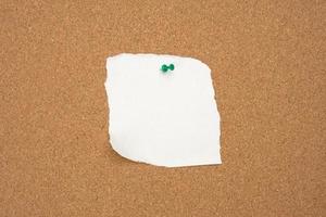 torn white blank white sheet of paper affixed with a plastic button on a brown cork board photo